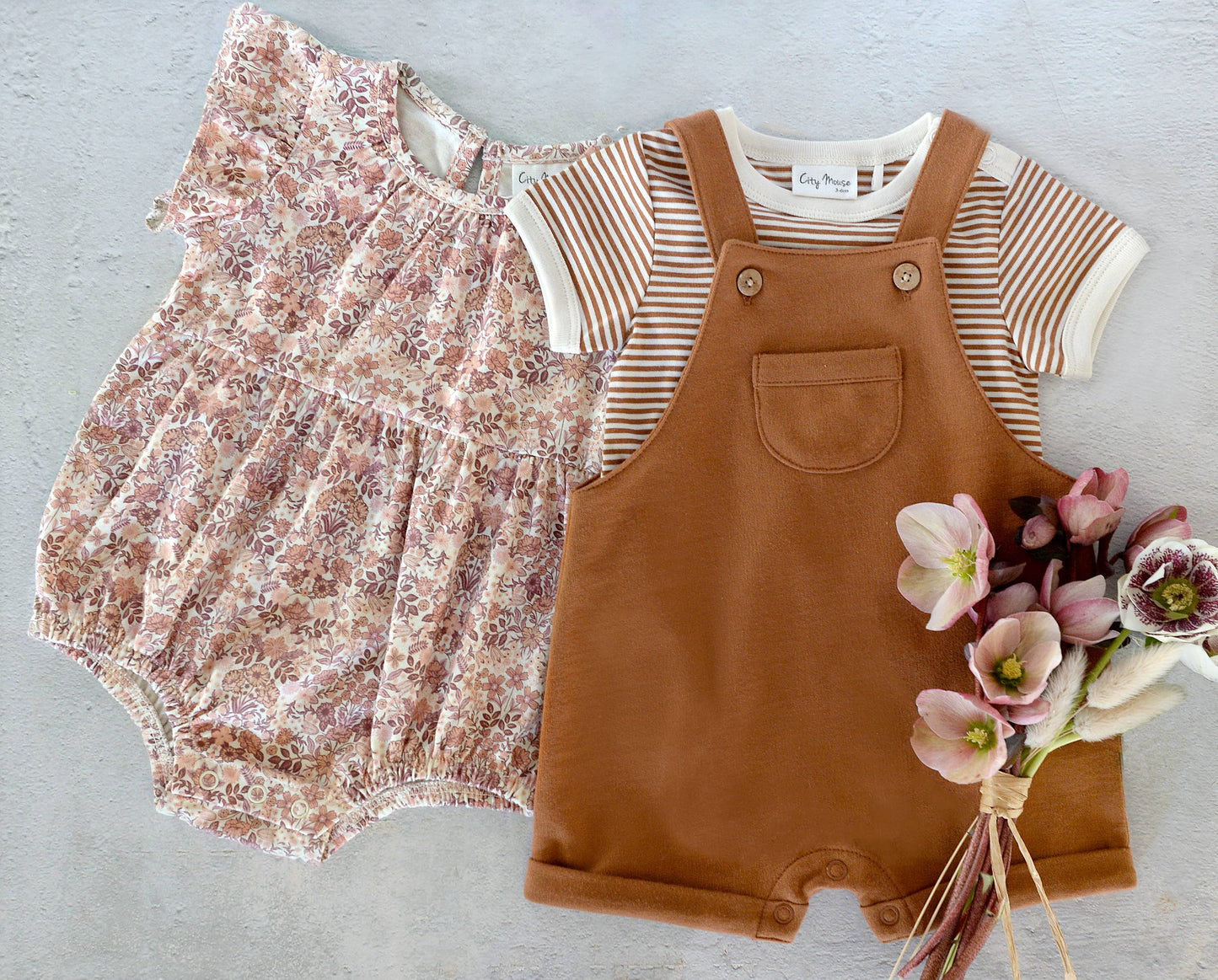 Baby romper, striped shirt, and brown overalls with a bouquet of flowers on a light gray background