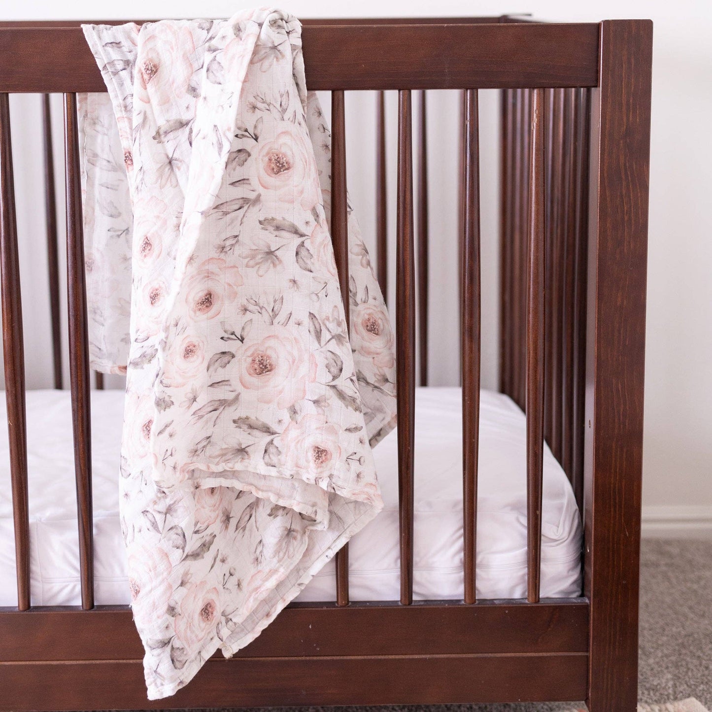 Floral blanket draped over a wooden crib with white bedding