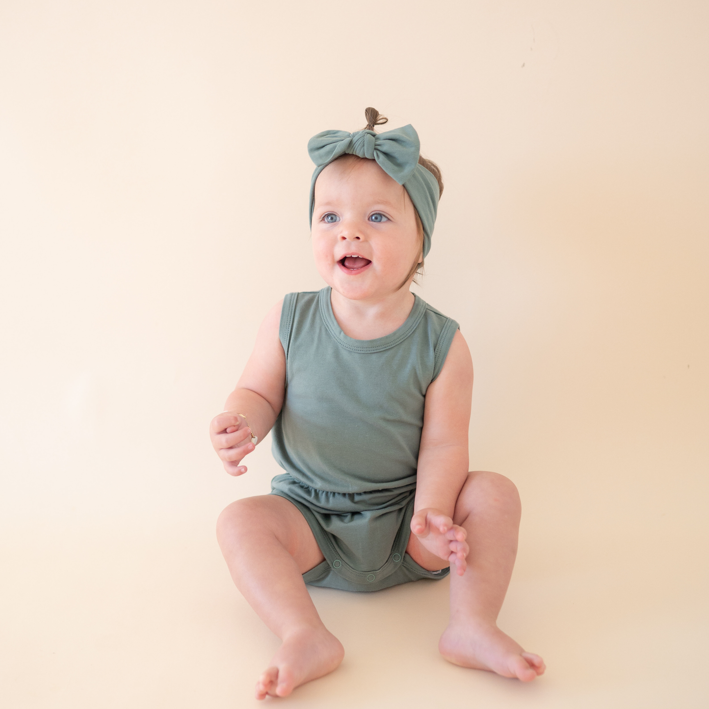 Baby wearing a green outfit and headband sitting on a beige surface