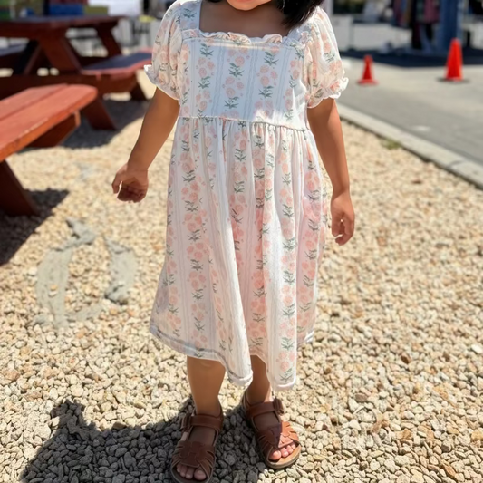 Young girl in a floral dress standing outdoors under a blue umbrella.