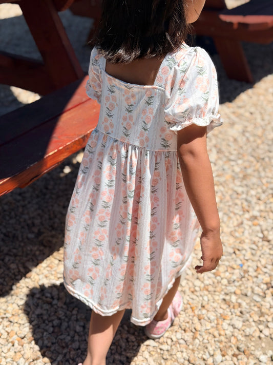 Child wearing a floral dress standing on a pebbled surface.