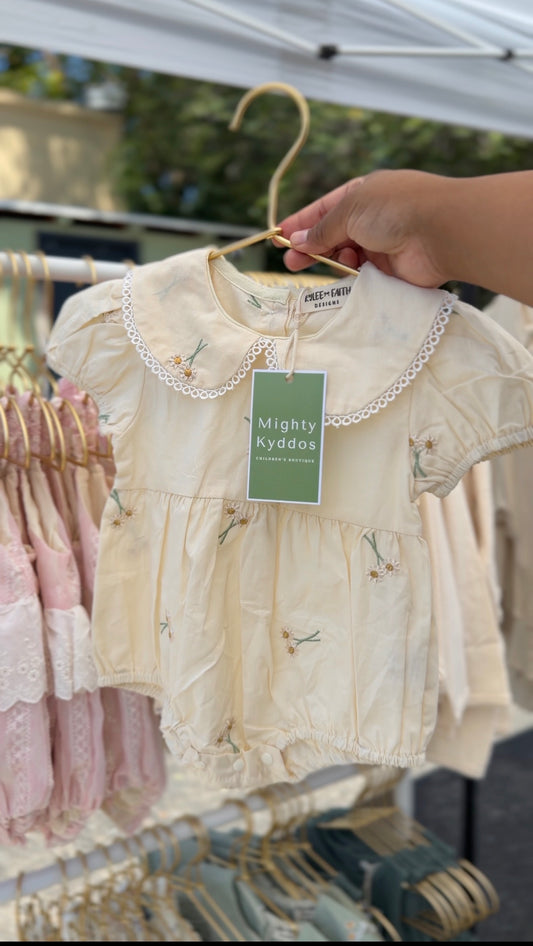 Baby dress on a hanger with a 'Mighty Kyddos' tag, held by a hand outdoors.