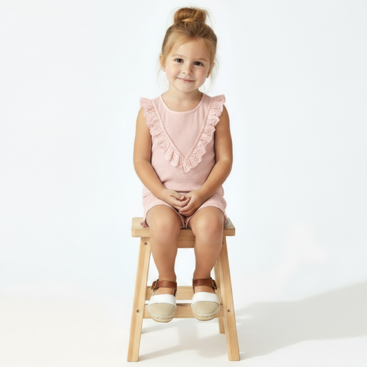 Girl in pink ruffled set sitting on a stool with a white background