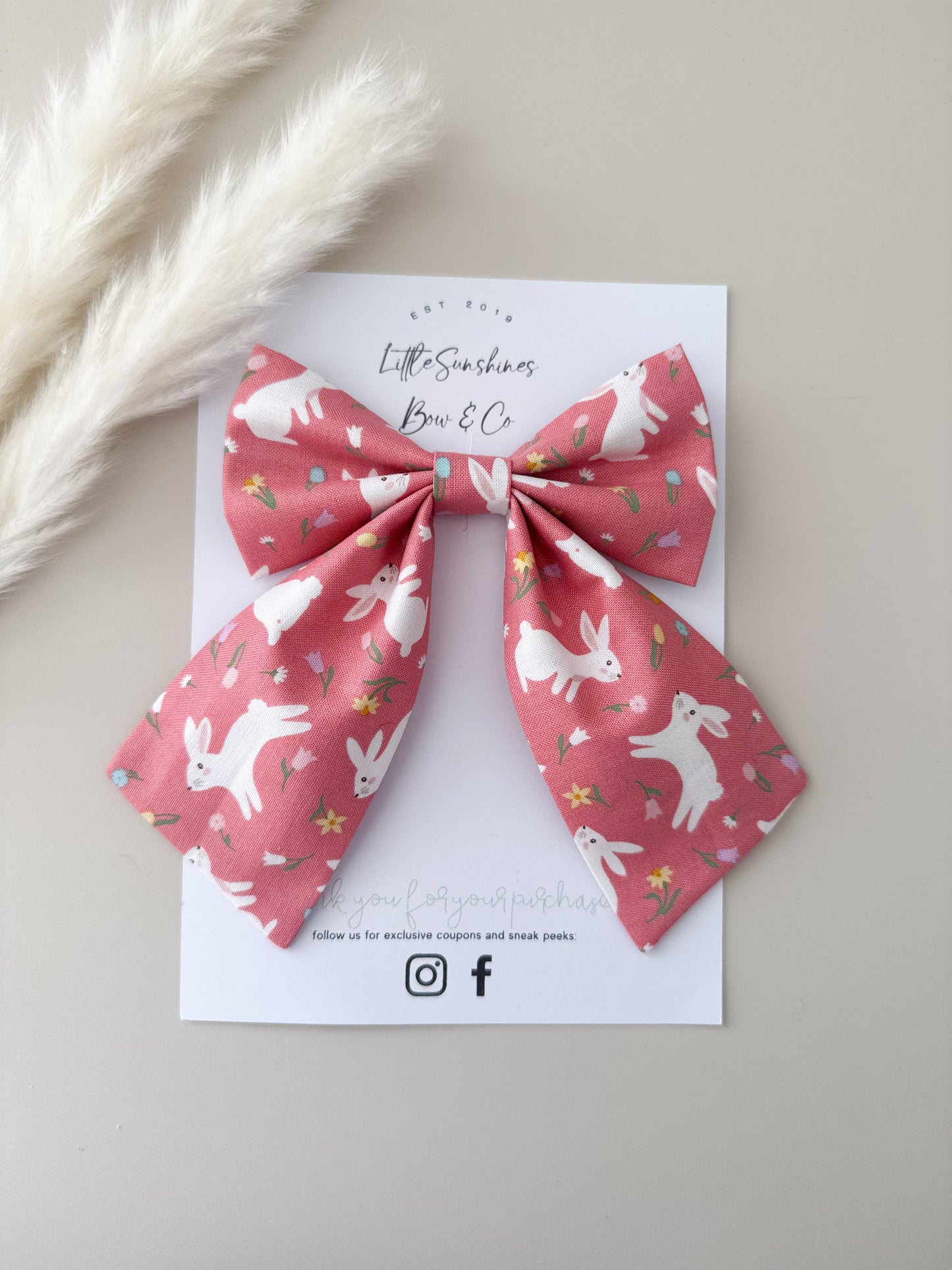 Pink bow with white rabbit pattern on a white card with branding, placed on a light gray background.