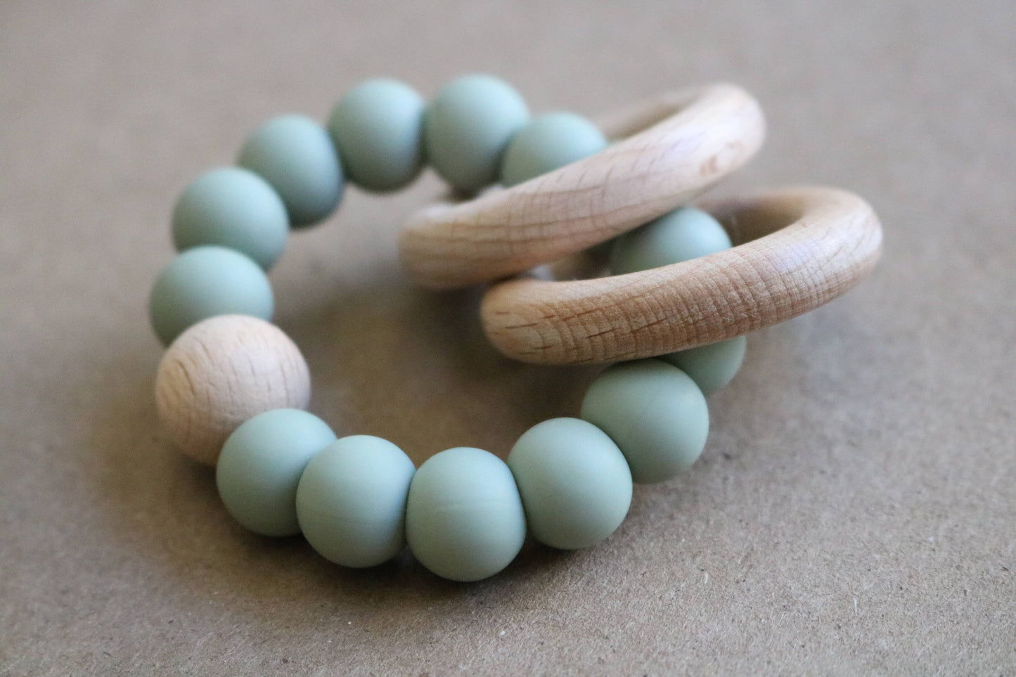 Teething ring with green beads and wooden rings on a beige background