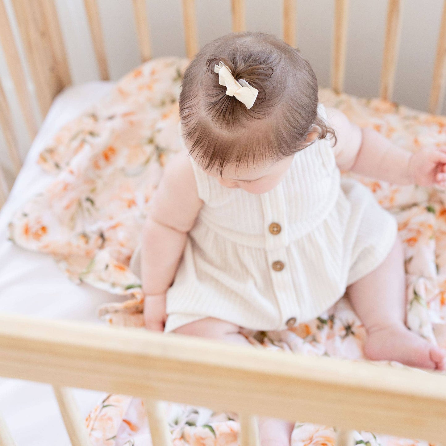 Baby in a crib with floral bedding and a white headband.