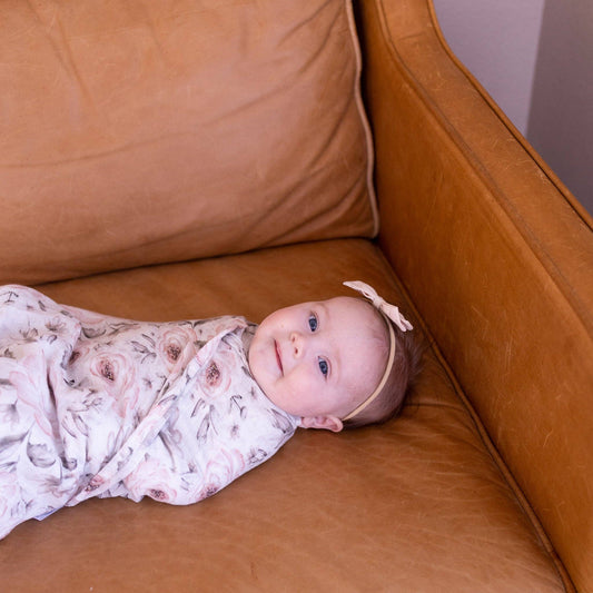 Baby swaddled in a floral blanket lying on a brown leather couch.