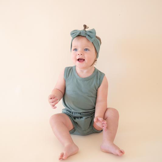 Baby wearing a green outfit and headband sitting on a beige surface