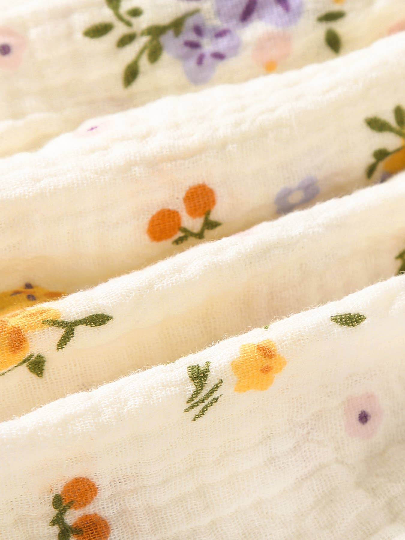Close-up of floral-patterned fabric with orange flowers and green leaves on a white background.