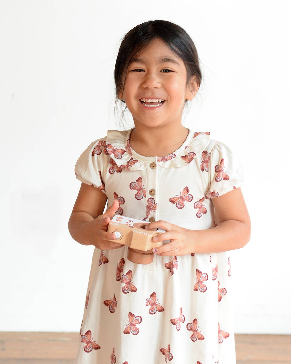 Young girl wearing a white dress with pink butterfly patterns on a white background