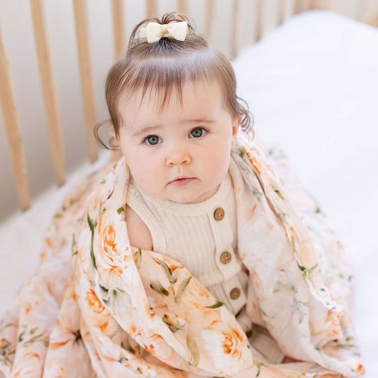 Baby wrapped in a floral blanket sitting in a crib