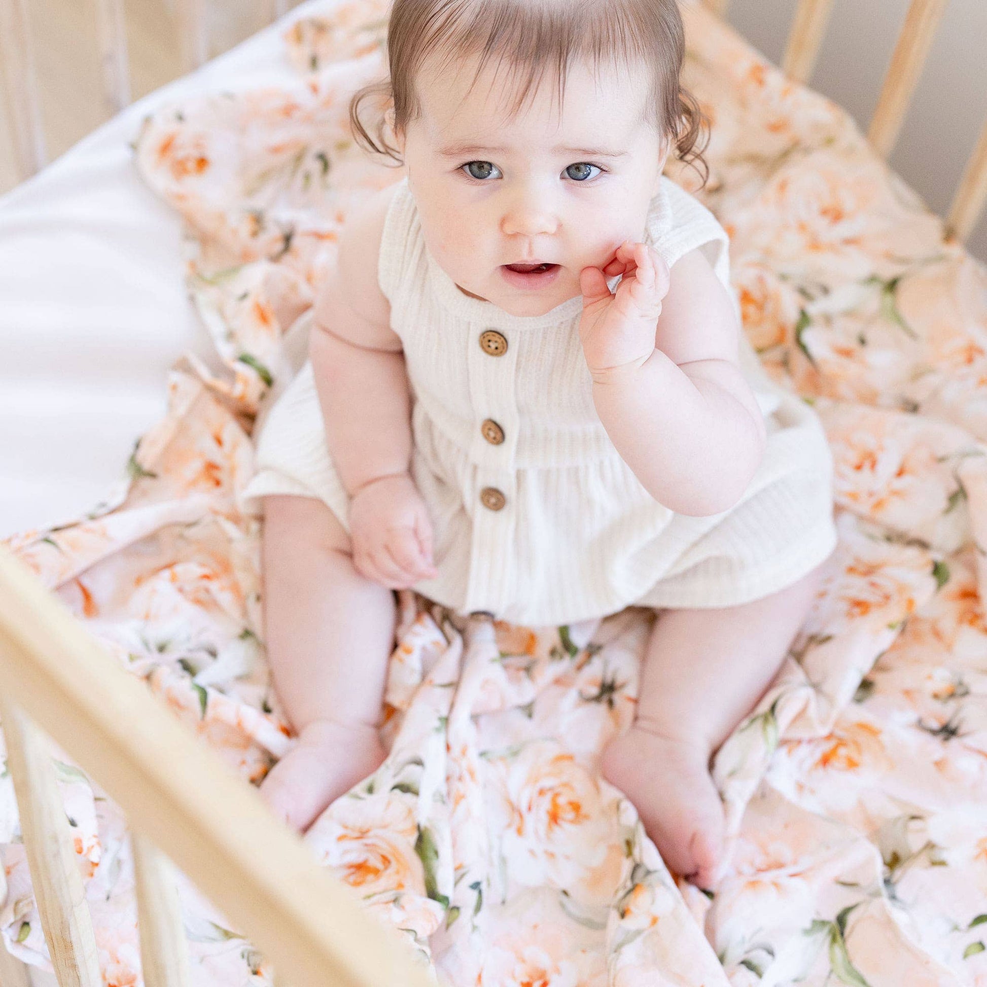 Baby sitting in a crib with floral bedding