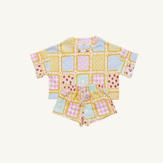A baby two-piece outfit set consisting of a short-sleeve top and matching shorts, featuring a colorful patchwork print with yellow, pink, blue, and white squares on a light cream background.