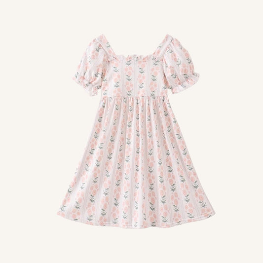 A white cotton dress with a pink floral print, featuring puff sleeves and a smocked bodice, shown against a plain off-white background.