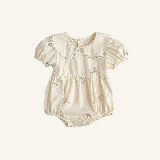 A cream-colored baby romper with short puff sleeves, a decorative lace Peter Pan collar, and small embroidered floral details, shown on a light beige background.