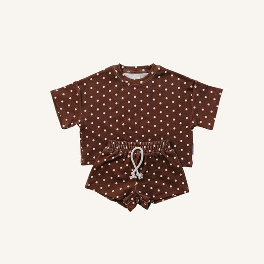 A baby two-piece clothing set consisting of a short-sleeve top and matching shorts in dark brown with a white polka dot pattern, displayed flat against a light cream background.