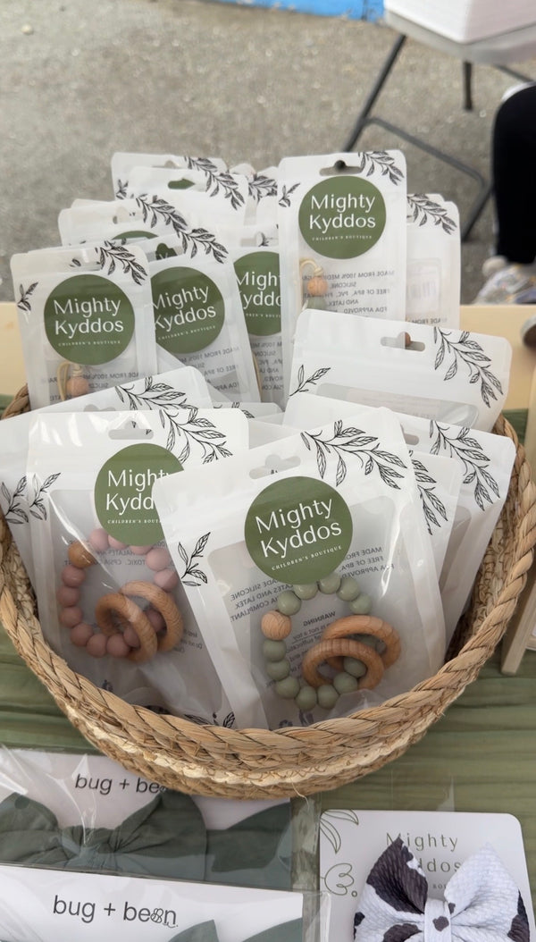 Basket of wood and silicone baby teethers in branded white packaging with sage green accents