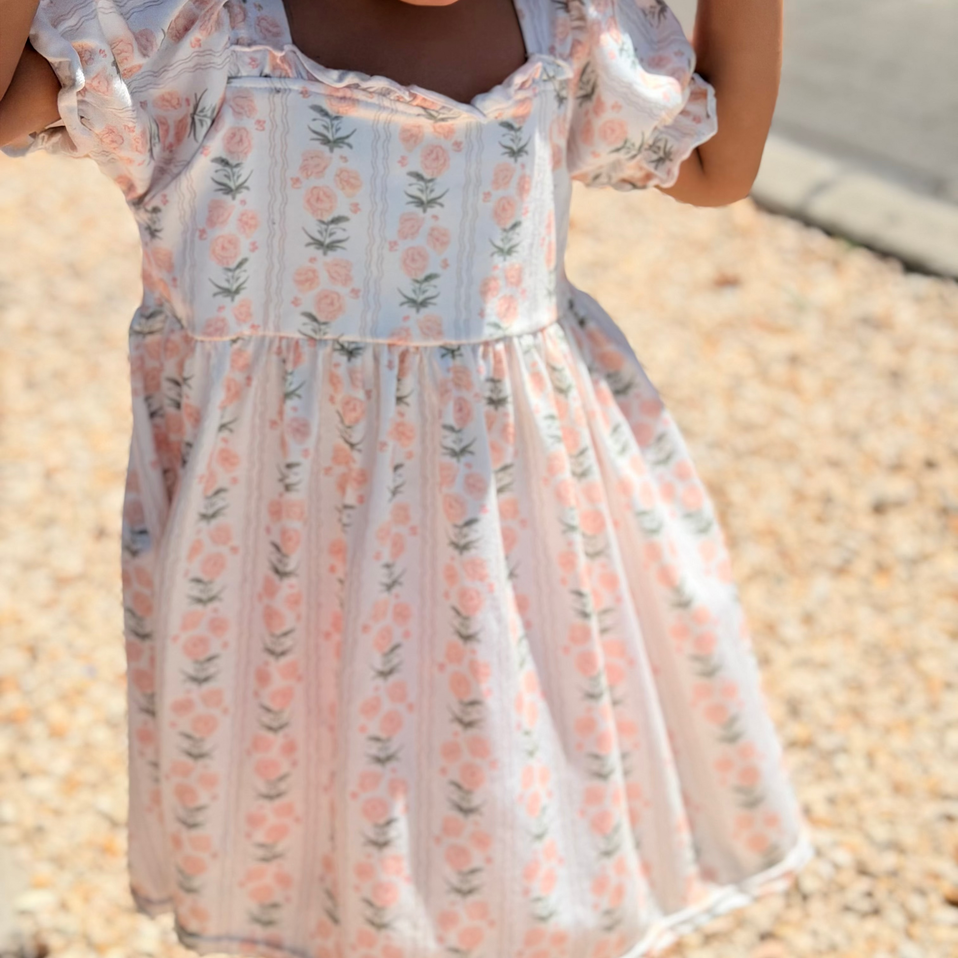 Child wearing a floral dress standing on a pebbled surface