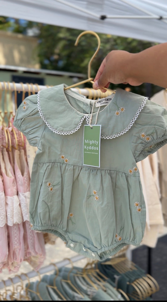 Green baby dress with floral embroidery on a hanger at an outdoor market.