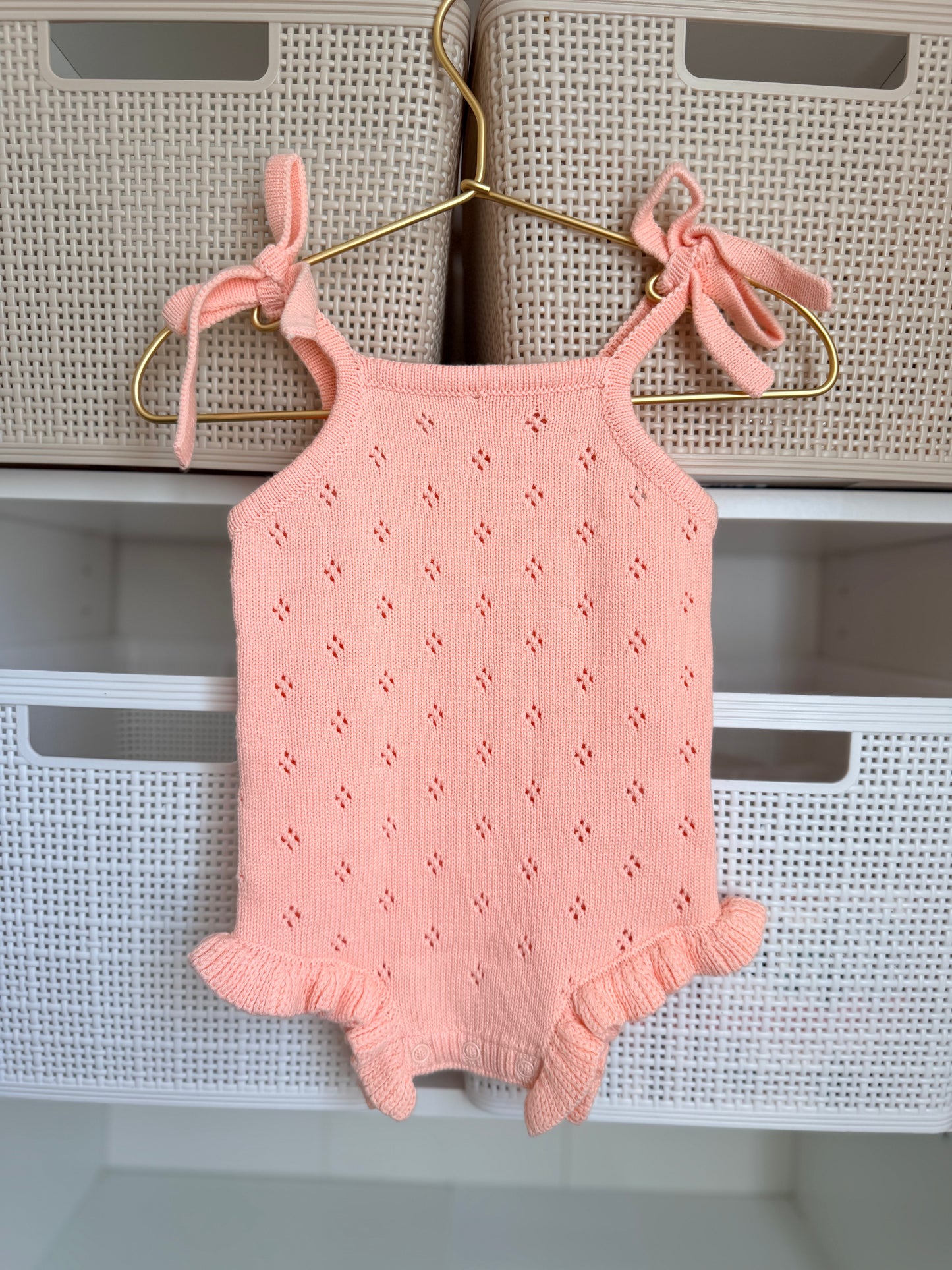 Pink baby romper with bow straps hanging on a hanger against a neutral background