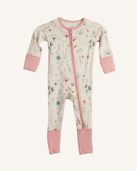Baby onesie with floral pattern and pink accents hanging on a white shelf with storage baskets.