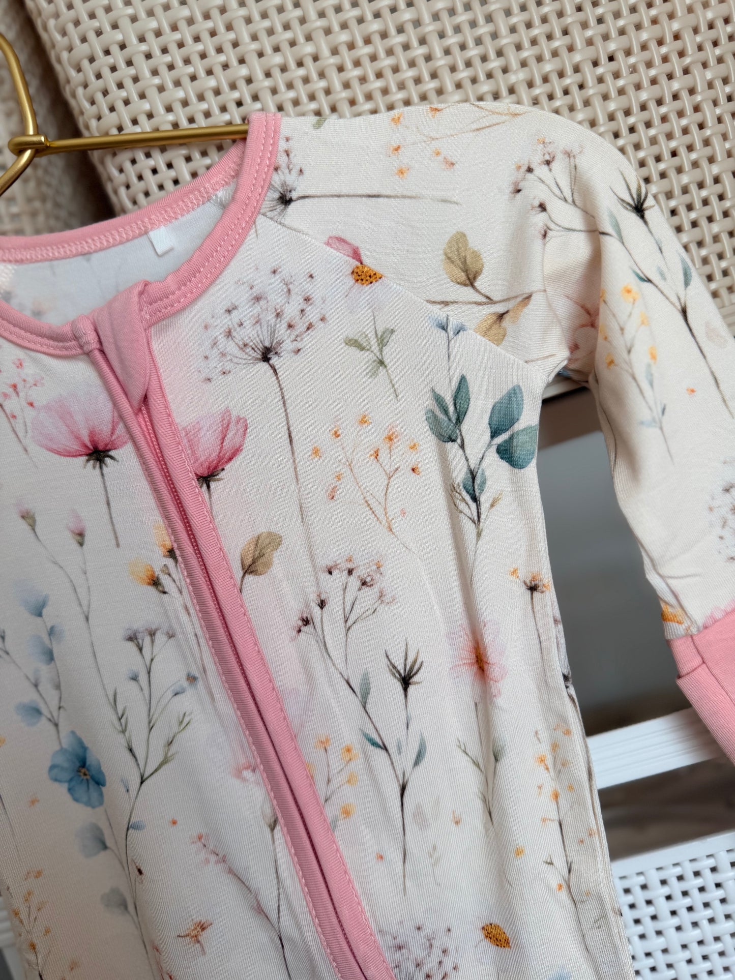 Baby romper with floral pattern and pink trim on a hanger.