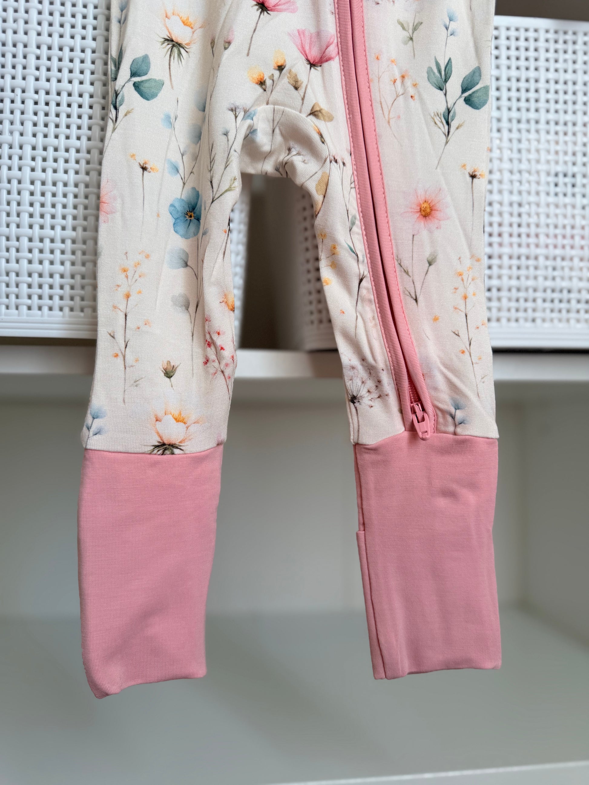 Floral-patterned baby romper with pink legs hanging on a white surface.