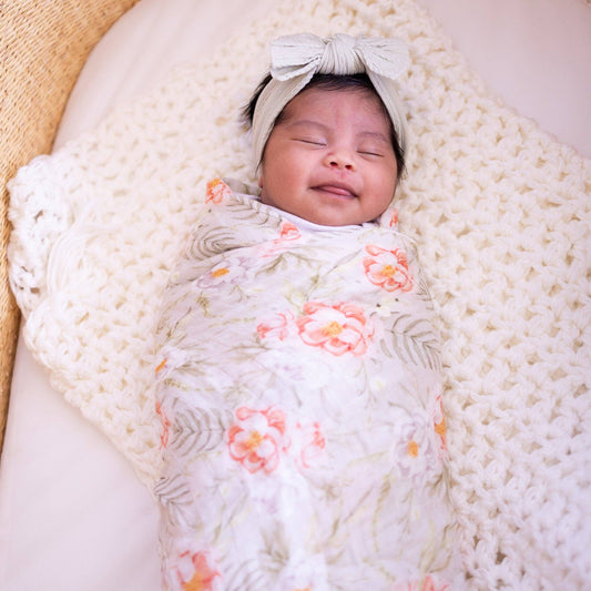 Newborn baby swaddled in a floral blanket with a bow on a white background