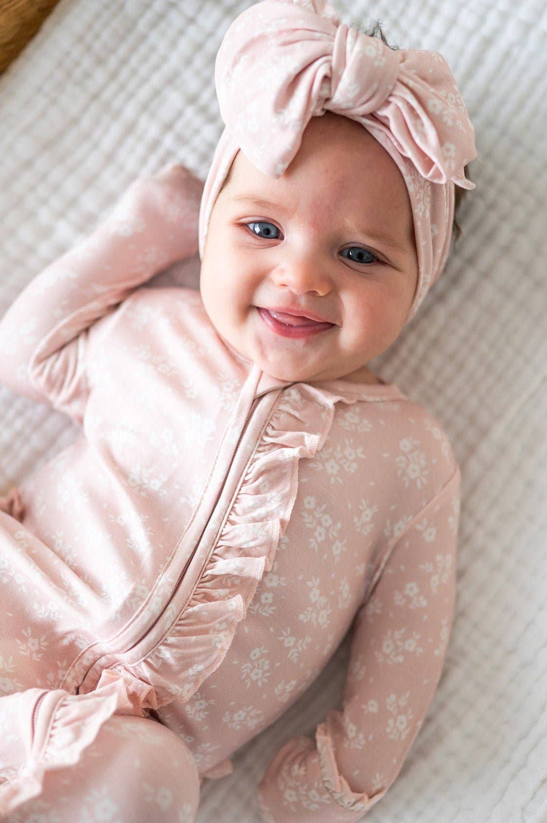 Baby in a pink outfit with a matching headband on a textured surface