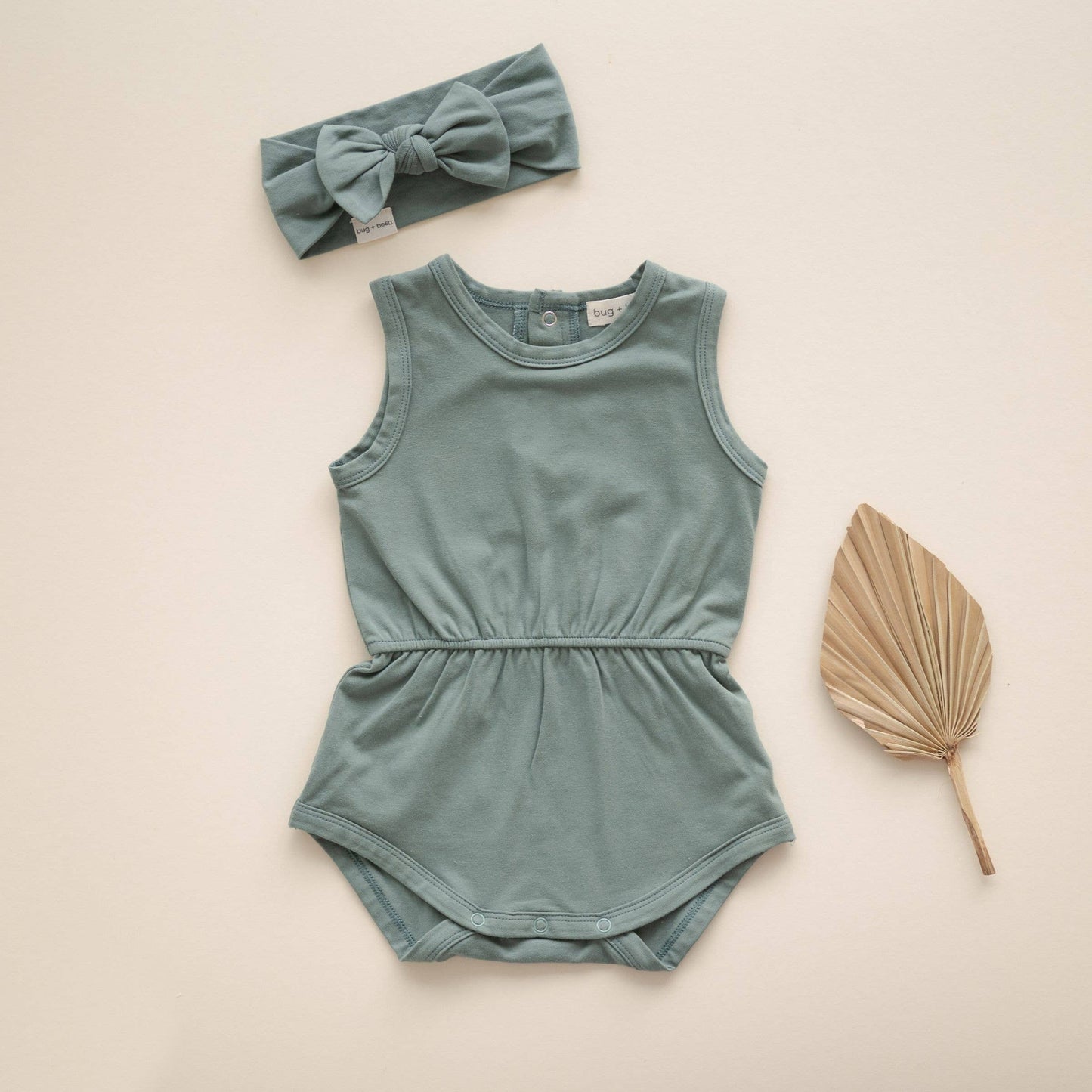 Green baby romper with matching headband and leaf on a beige background