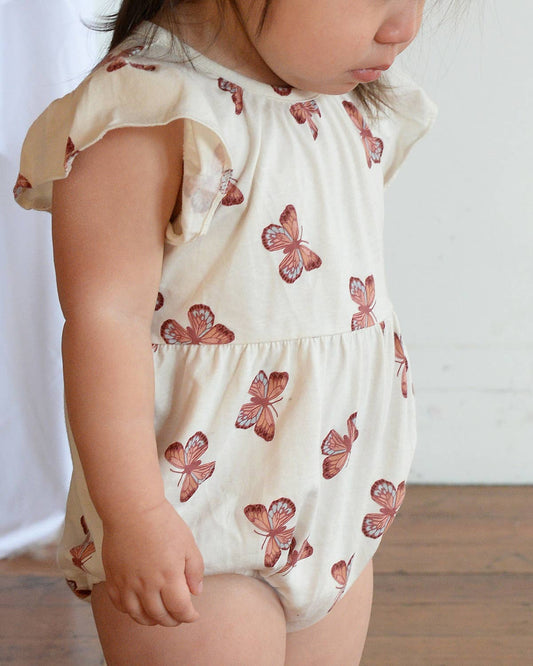 Child wearing a white romper with red butterfly patterns on a plain background