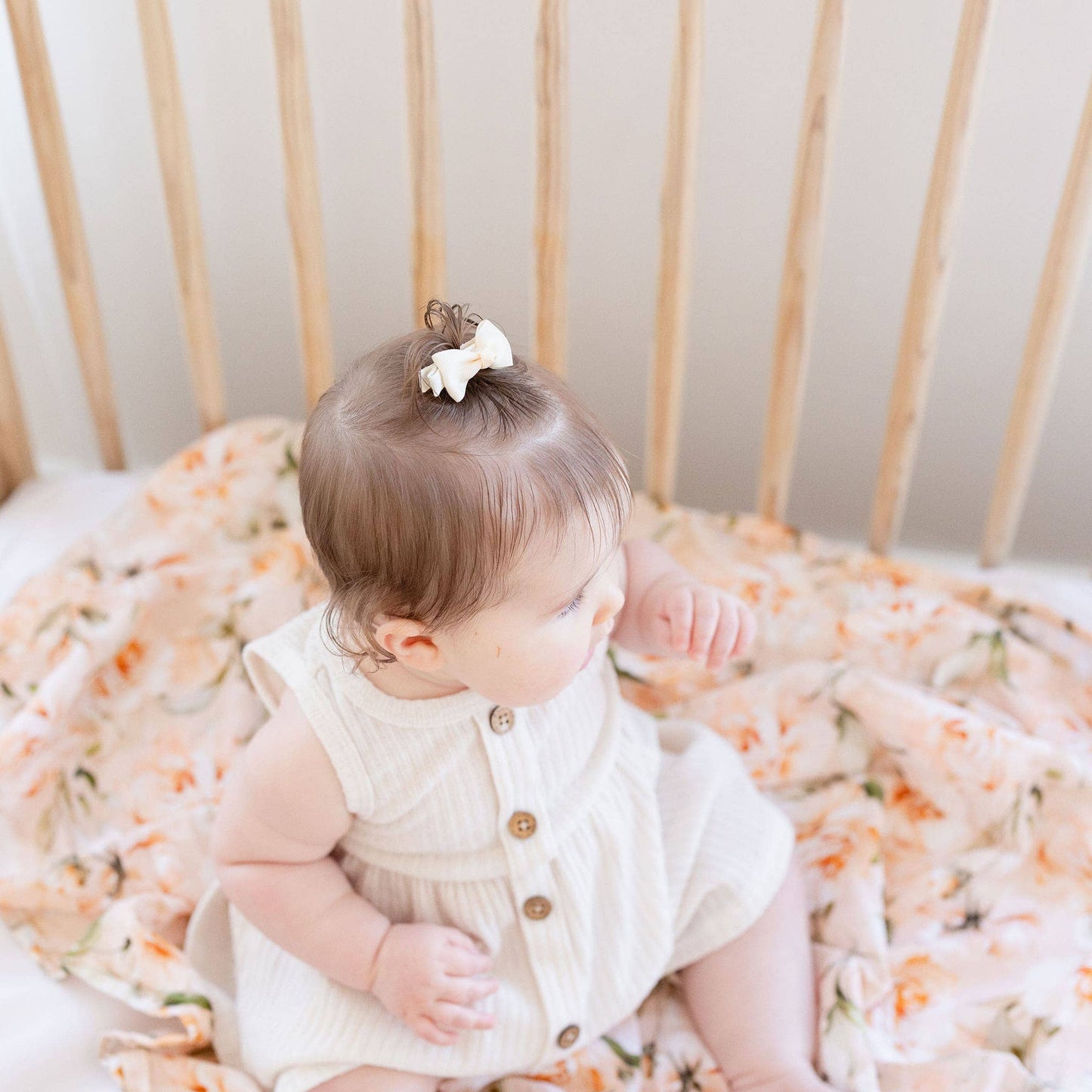 Baby sitting in a crib with floral bedding