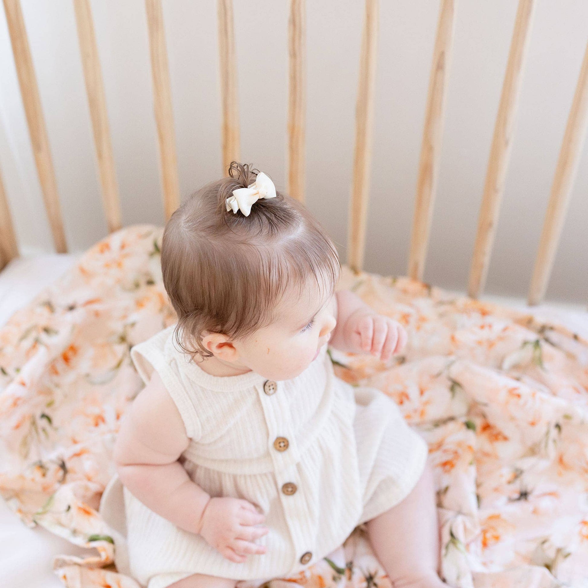 Baby sitting in a crib with floral bedding
