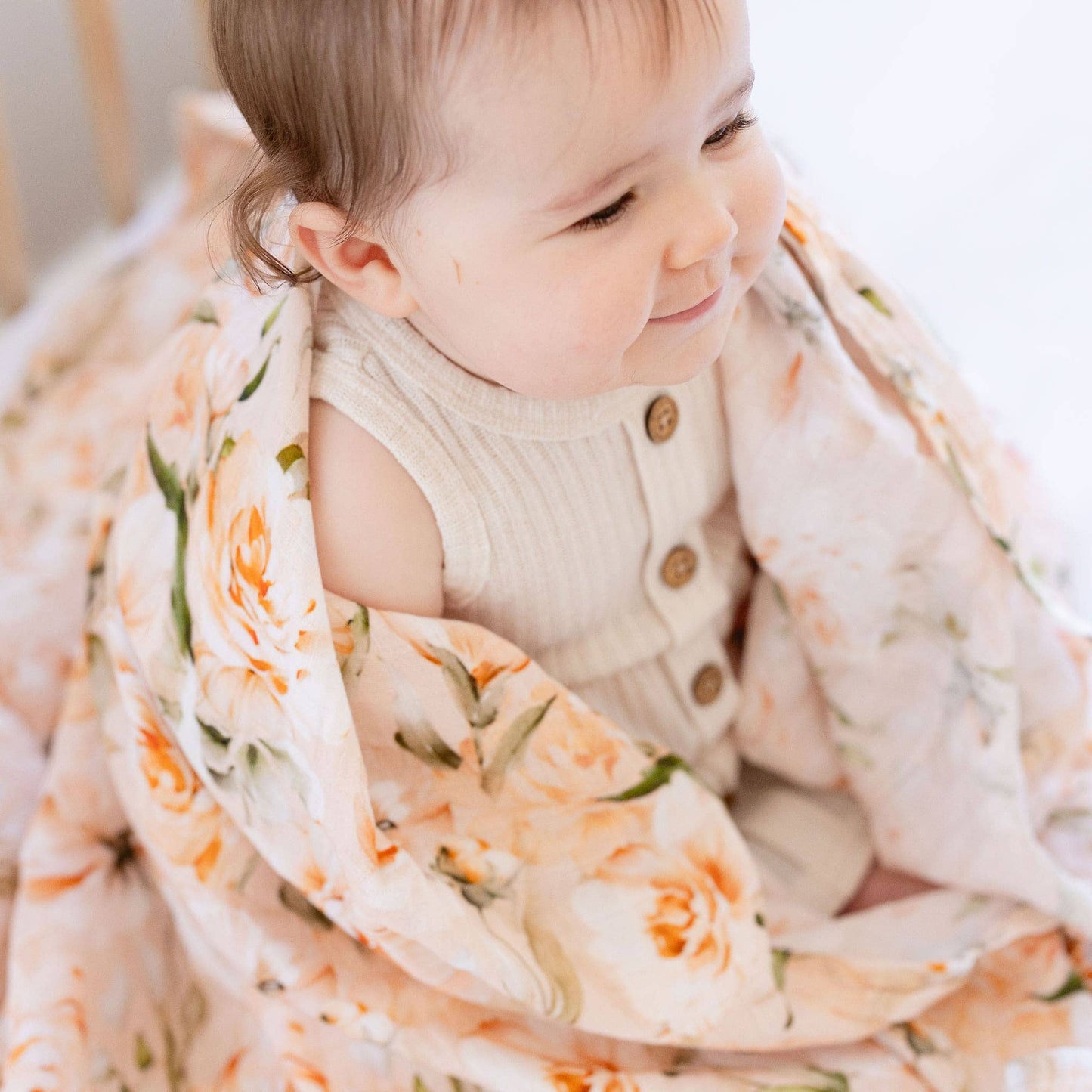 Child wrapped in a floral blanket with a neutral background