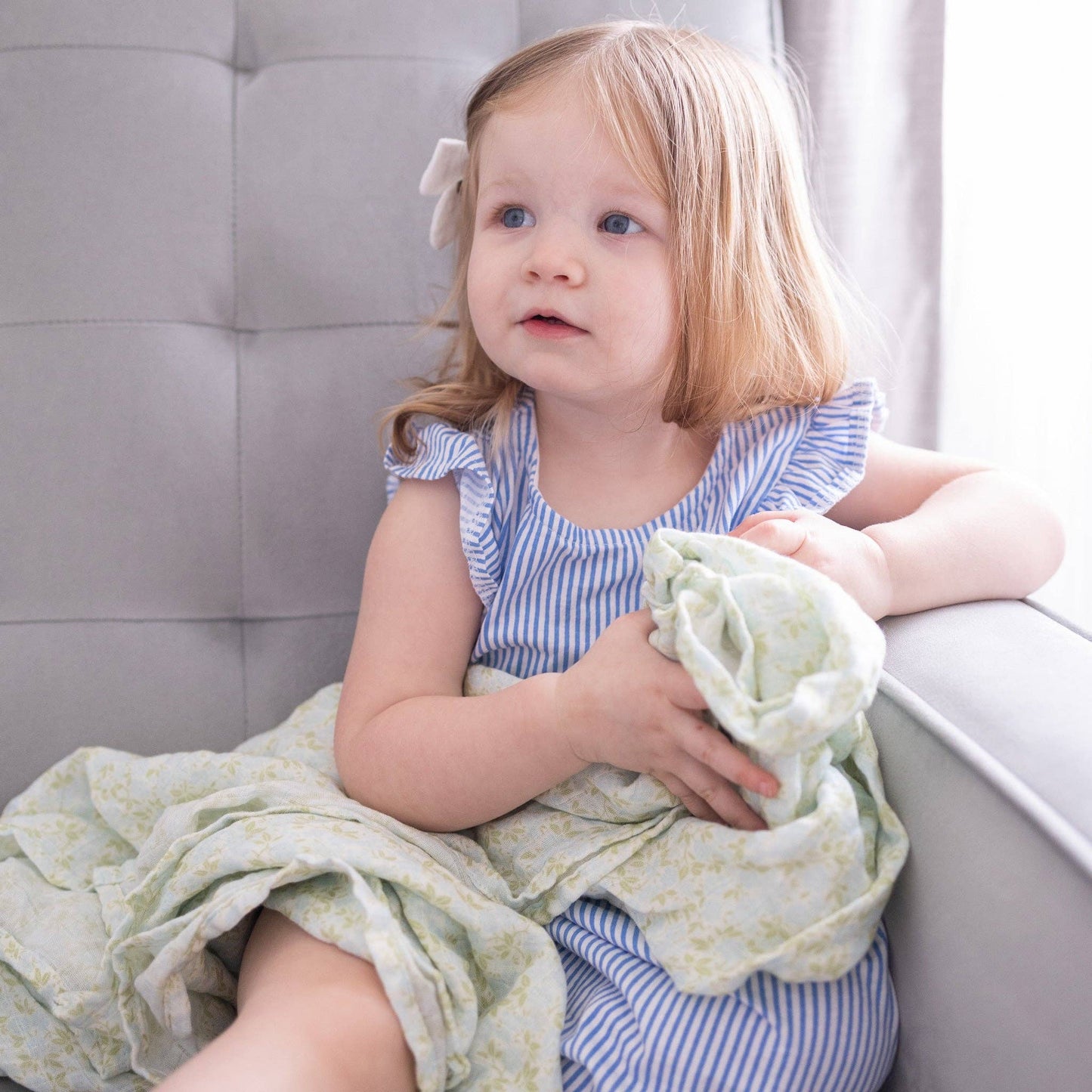 Young girl holding a green blanket in a neutral setting