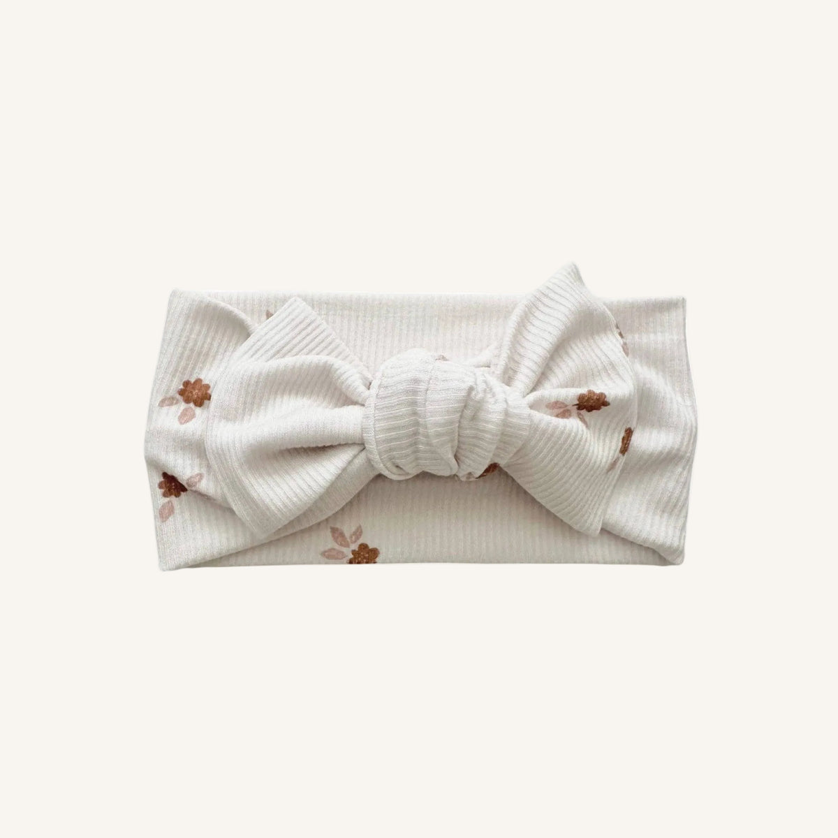 An off-white ribbed fabric headband with a large bow in the center and small brown floral prints, shown on a plain white background.