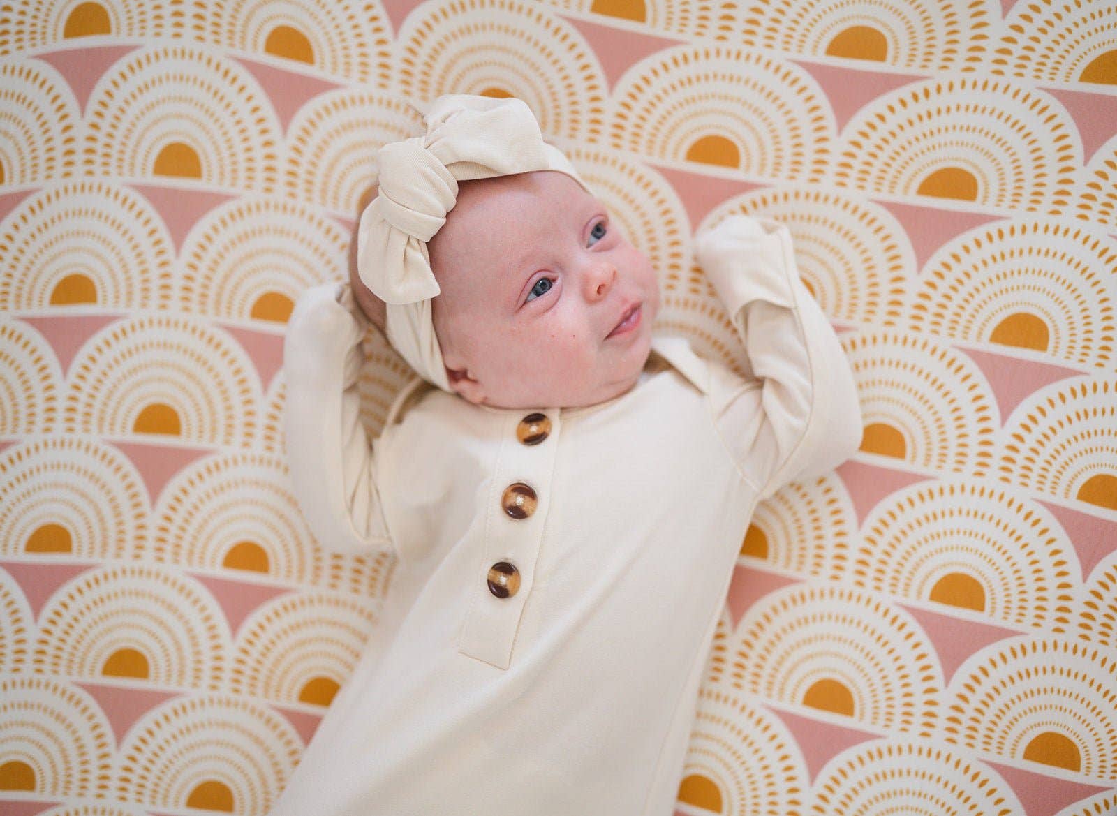 Newborn baby in a white outfit with brown buttons on a pink and yellow patterned blanket