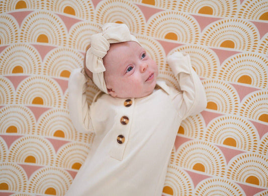 Newborn baby in a white outfit with brown buttons on a pink and yellow patterned blanket