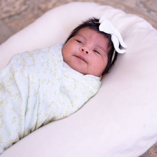 Newborn baby swaddled in a light blue blanket with a white bow on a neutral background
