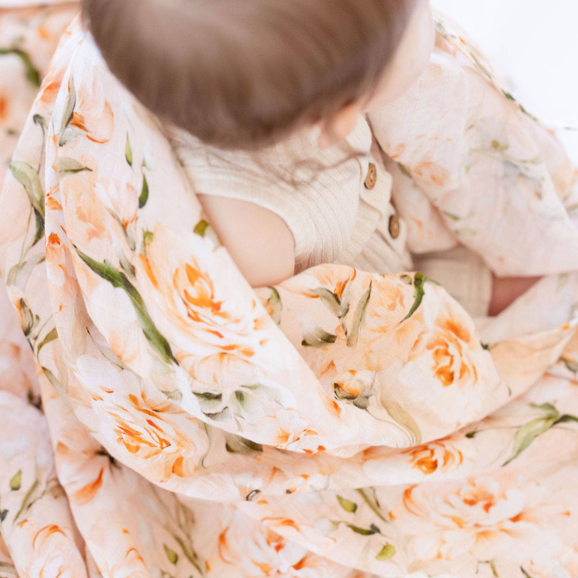 Baby wrapped in a floral blanket with orange roses on a white background
