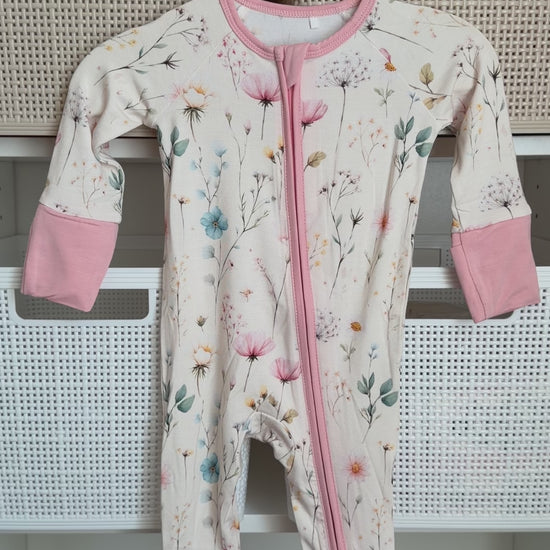 Floral-patterned baby onesie with pink accents hanging on a white rack.