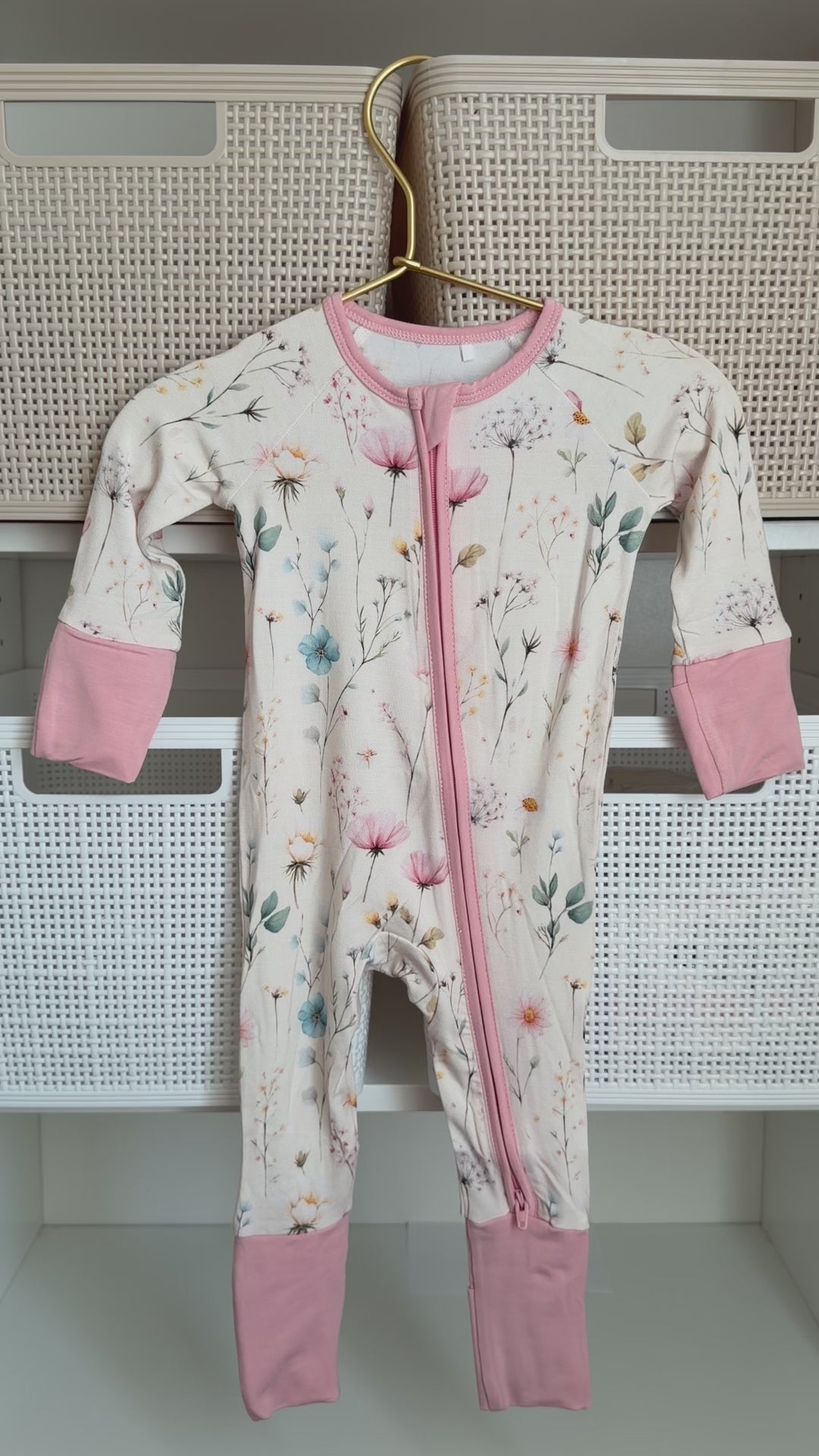 Floral-patterned baby onesie with pink accents hanging on a white rack.