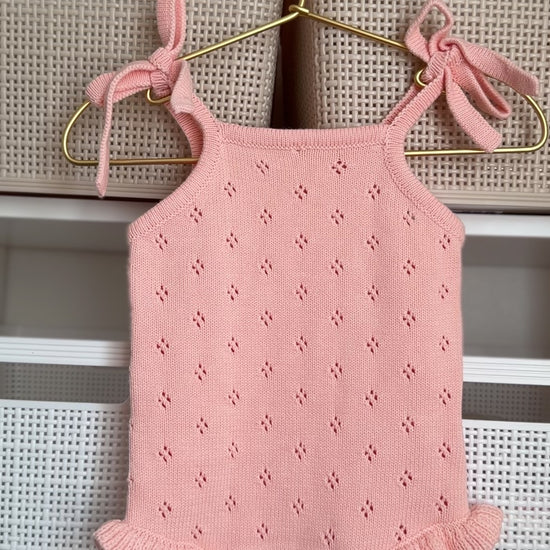 Pink baby romper with bow straps hanging on a hanger against a neutral background