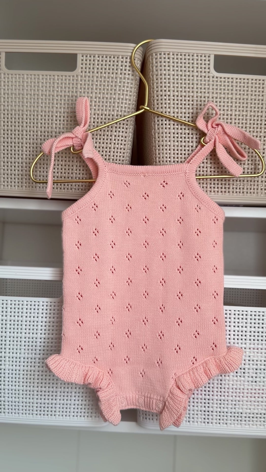 Pink baby romper with bow straps hanging on a hanger against a neutral background